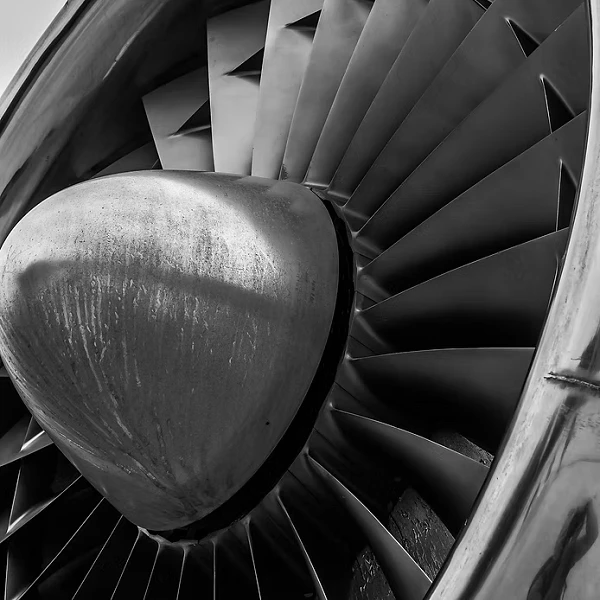 Nahaufnahme eines Flugzeugtriebwerks mit gut sichtbaren, geschwungenen Turbinenblättern und einer reflektierenden metallischen Oberfläche.