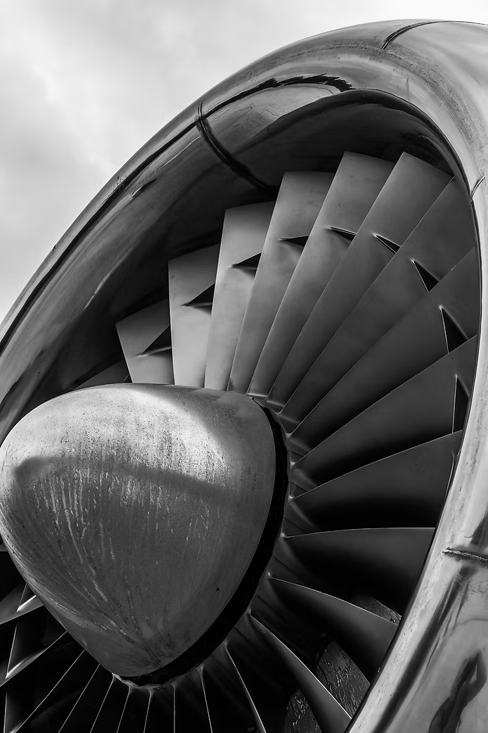 Nahaufnahme eines Flugzeugtriebwerks mit gut sichtbaren, geschwungenen Turbinenblättern und einer reflektierenden metallischen Oberfläche.